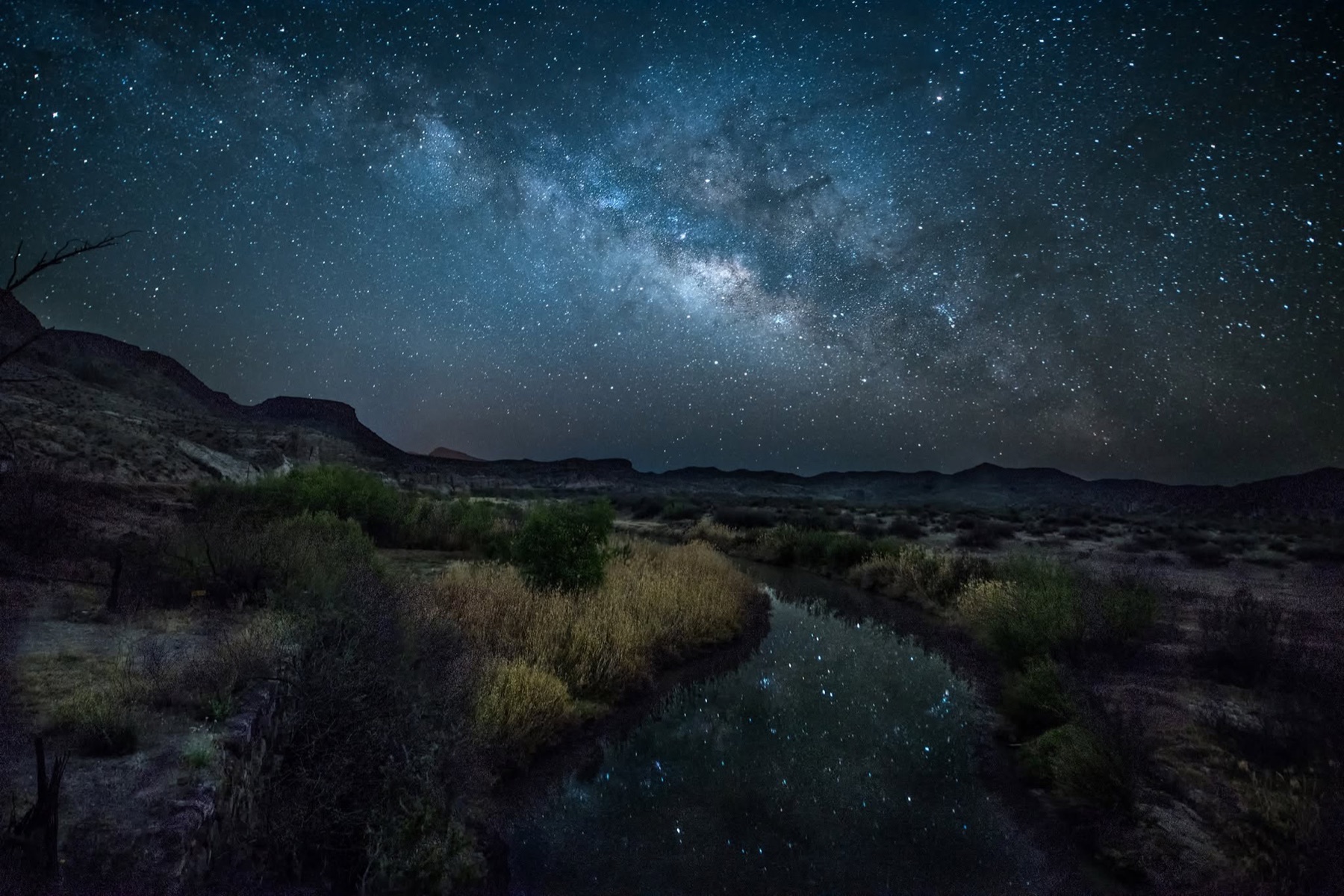 The Milky Way stretching over a dark desert river landscape in Big Bend
