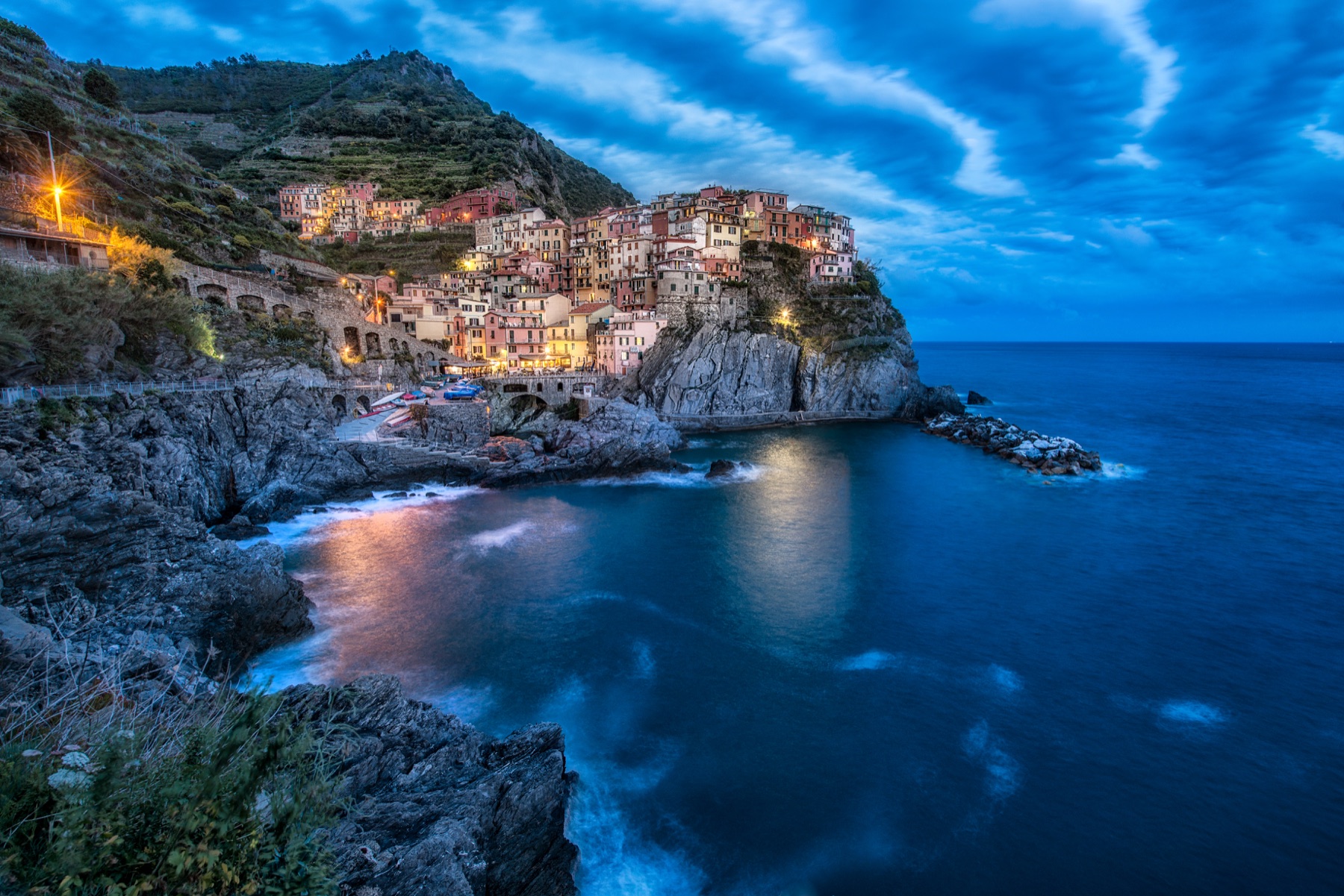 The colorful village of Manarola glowing above the blue sea at twilight