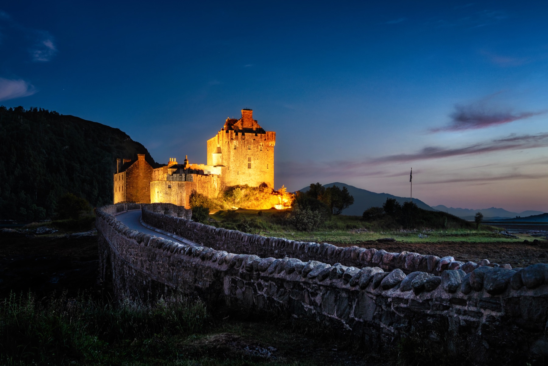 Eilean Donan Castle illuminated at twilight beyond a stone wall