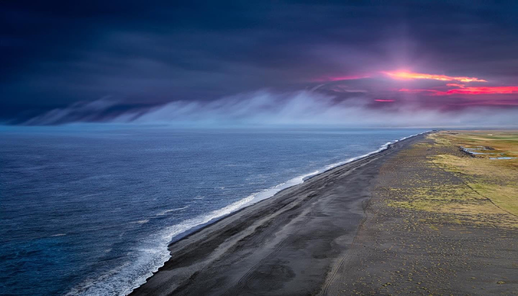 A long black Icelandic coastline under a purple storm break
