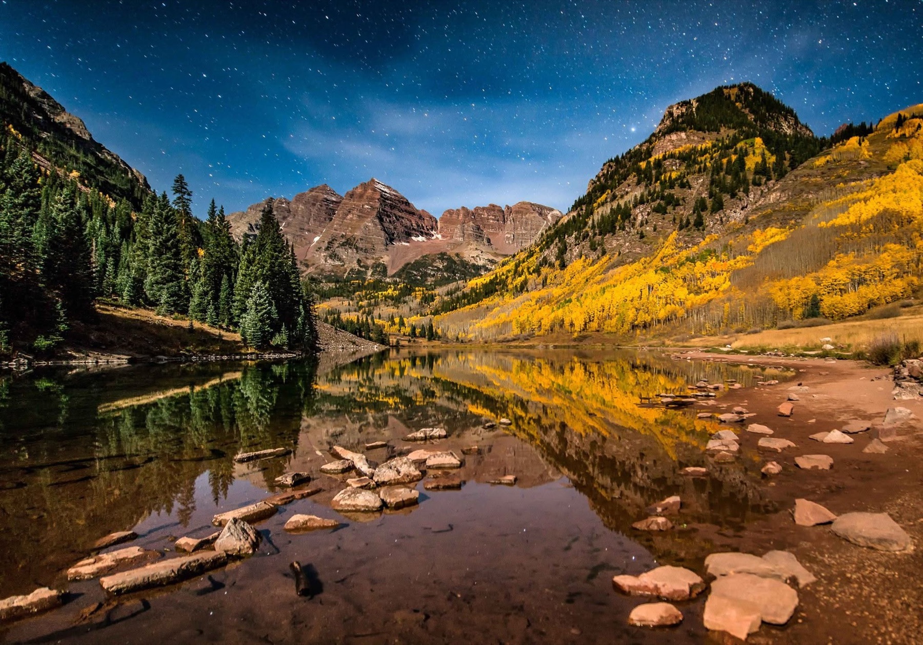 Maroon Bells and autumn aspens reflected beneath a star-filled blue sky