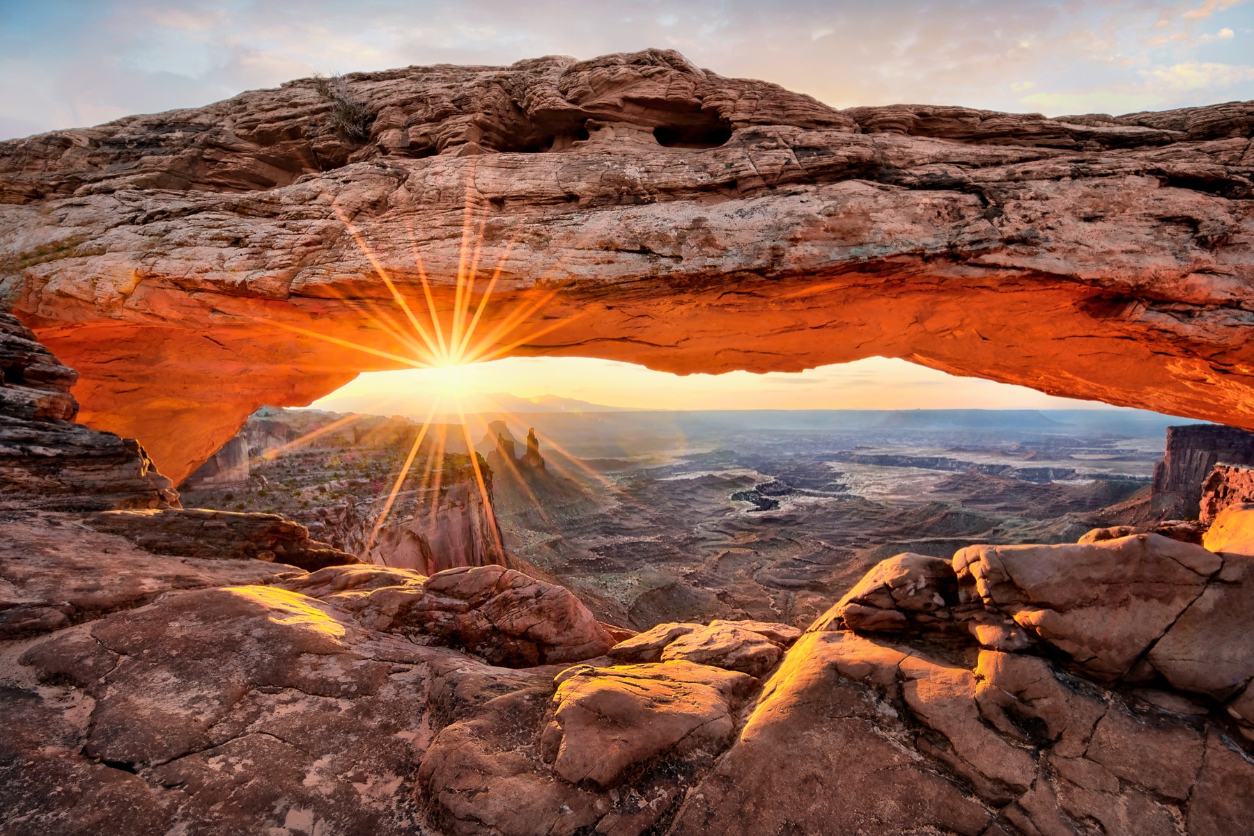 Sunlight forming a starburst beneath Mesa Arch above a canyon