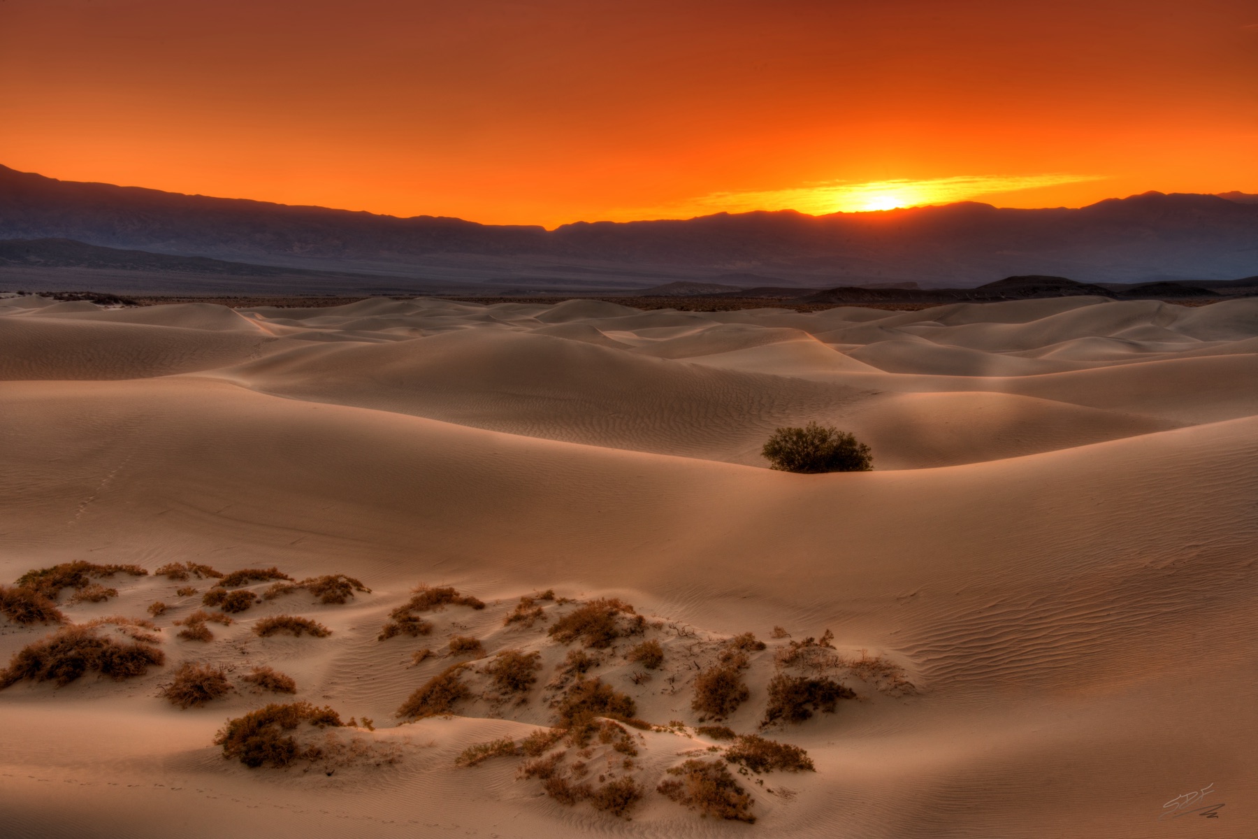 A red sunset slipping behind distant mountains and pale desert dunes