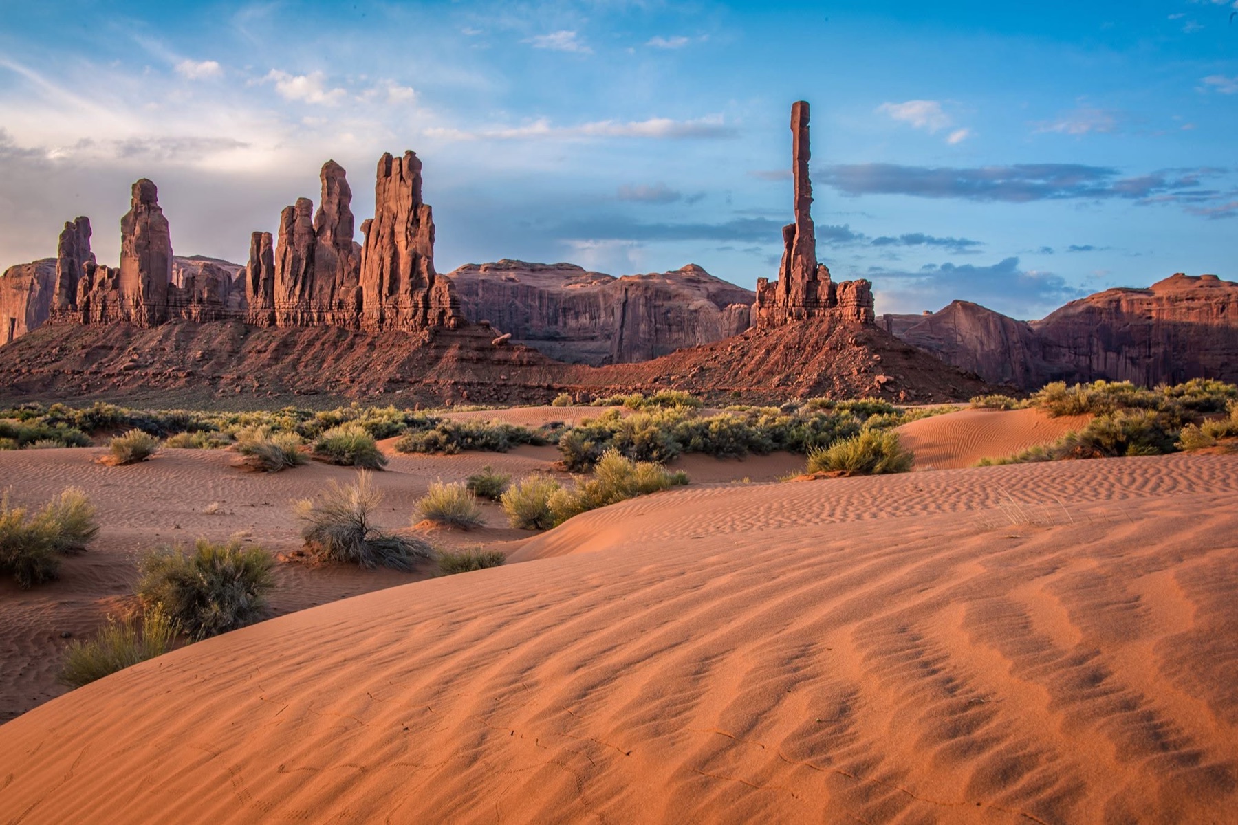 Monument Valley towers rising beyond warm wind-rippled sand