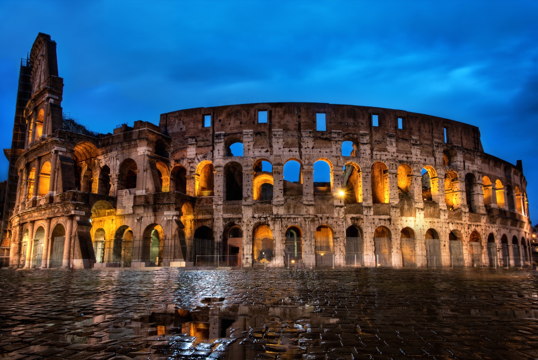 The Roman Colosseum glowing at blue hour and reflected in rainwater