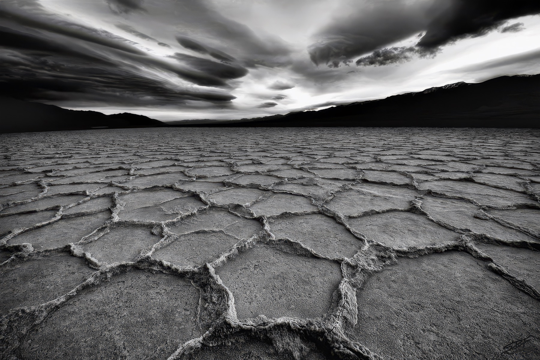 Black and white salt polygons stretching toward dark mountains beneath racing clouds