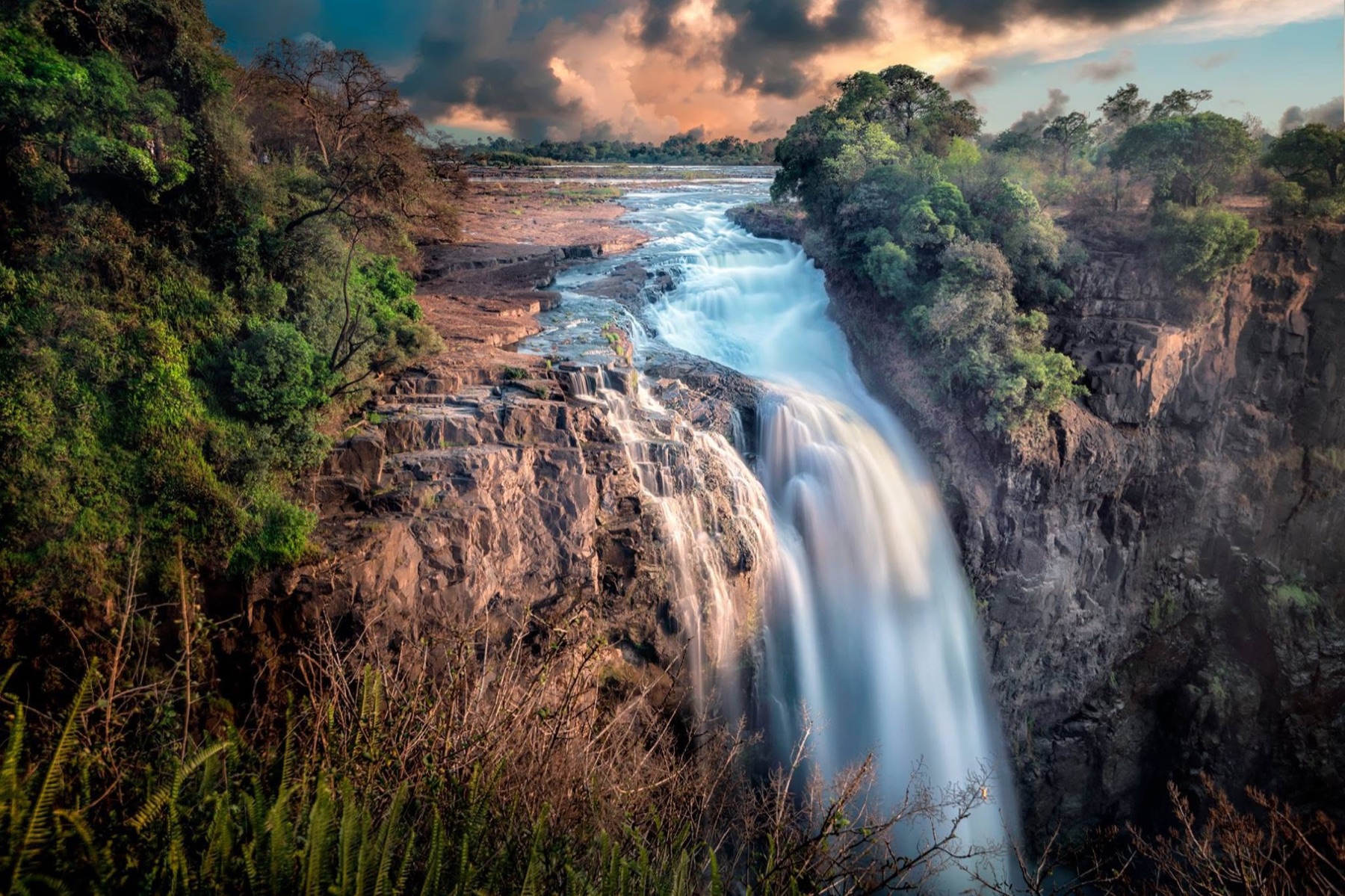 Victoria Falls dropping through a deep gorge beneath warm storm light
