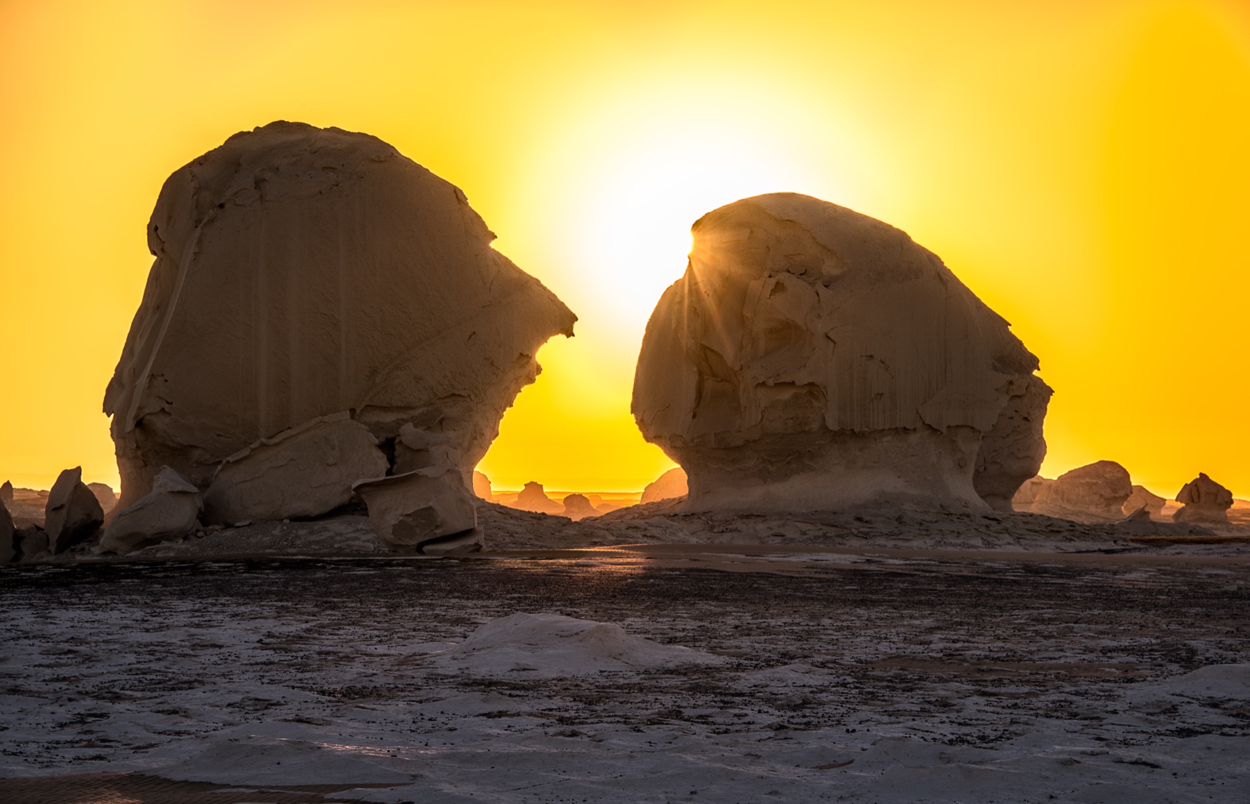 Two large White Desert formations silhouetted against a yellow sunset