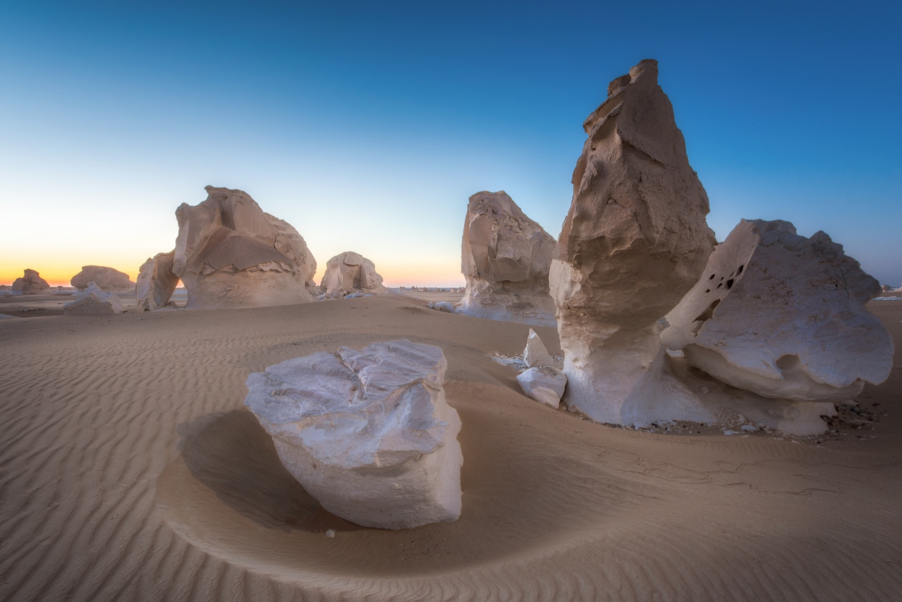 Sculptural white chalk formations rising from pale desert sand at dusk